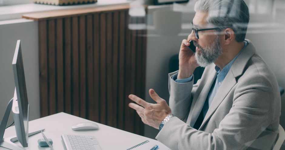 Senior businessman speaking on phone at desk in a modern office setting